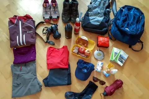 Packliste Wandern Mehrtagestour: Kleidung, Rucksäcke, Kamera, Verpflegung, Trinkflasche, Schuhe, Hut, Sonnenbrille, Regenschirm und Karten für die Tour.