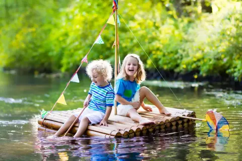 Zwei Kinder bauen einen Floss und genießen den Sommer auf dem Wasser.