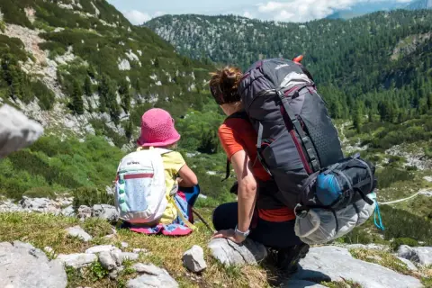 Mutter und Kind genießen die Aussicht beim steinernes Meer wandern. Die beiden sitzen auf einem Felsen, umgeben von grüner Natur und Bergen.
