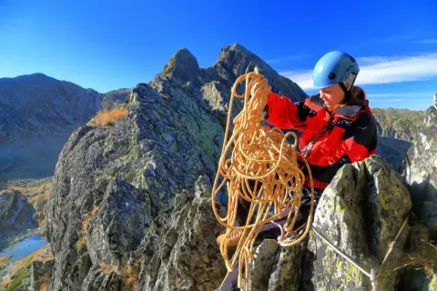 Bergsteigerin mit Seil in den Bergen, bereitet sich auf das Klettern vor und achtet auf wichtige Knoten.