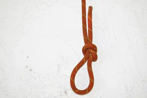 Ein orange-gelbes Seil bildet einen Knoten, der sich zuzieht, vor einer weißen, strukturierten Wand.