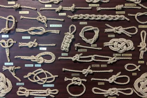 Eine Tafel mit vielen verschiedenen Knoten und ihren Namen. Von einfachen Schlaufen bis zu komplexen Seemannsknoten, hier sind die Knoten Namen zu sehen.