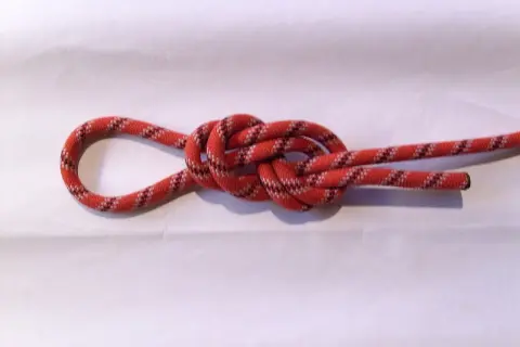 Ein rotes Seil mit schwarzen und weißen Mustern bildet einen Achterknoten, der sicher und stabil aussieht.