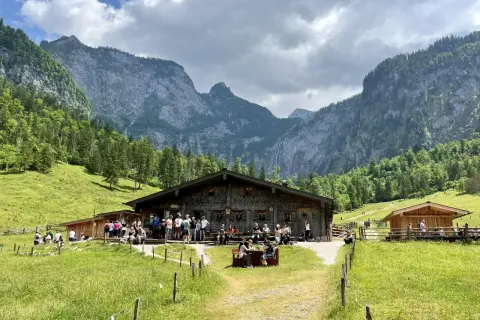 Eine Berghütte mit Gästen vor einer beeindruckenden Bergkulisse, die an ein steinernes Meer erinnert.