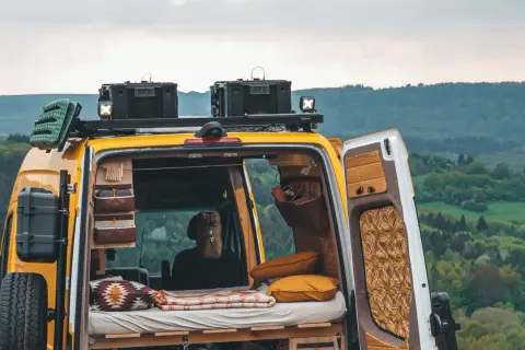 Gelbes Campervan mit gemütlichem Innenraum, bereit für wildcampen in Europa. Dachgepäckträger, Ersatzrad und Stauraum für Abenteuer.
