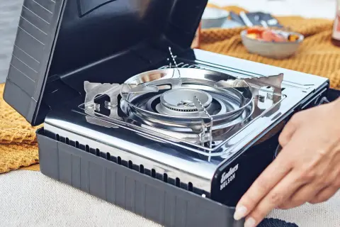 Ein Campingkocher mit offenem Deckel, bereit für die Zubereitung von Speisen. Die richtige Lagerung von Gaskartuschen ist wichtig für die Sicherheit.