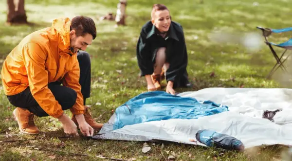 Mann und Frau bereiten ihr Zelt vor. Sie legen die Zeltplane aus, um das Zelt zu reinigen und aufzubauen.