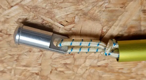 Detailaufnahme: Ein silbernes Endstück mit einer Öse ist mit einem elastischen Seil verbunden, das in ein gelbes Rohr führt. Dies ist eine Methode, um eine Zeltstange zu reparieren.