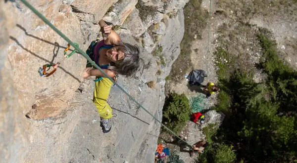 Frau klettert an einer Felswand bei Briançon, während unten ein Team wartet.