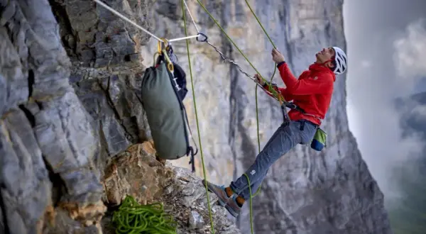 Bergsteiger sichert den nachstieg an der Felswand. Seile, Rucksack und Ausrüstung sind sichtbar.