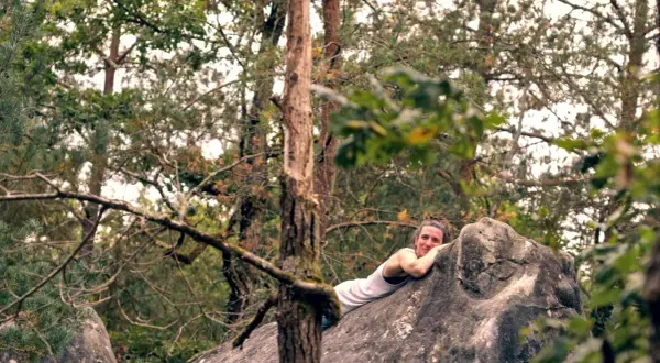 Frau ruht sich nach dem Fontainebleau Bouldern auf einem Felsen aus, umgeben von Bäumen.