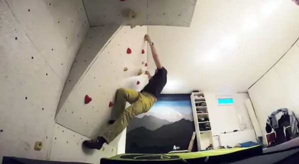 Mann klettert an einer selbstgebauten Boulderwand. Bunte Griffe sind auf der Wand verteilt.