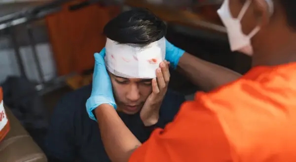 Sanitäter versorgt eine Platzwunde am Kopf eines jungen Mannes mit Verband.
