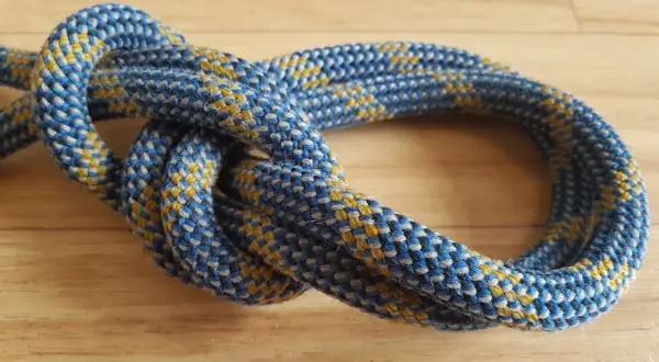 Eine detaillierte bulin knoten anleitung zeigt, wie man diesen sicheren Knoten knüpft. Das Seil ist blau-gelb gemustert.