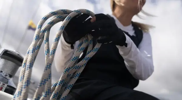 Seglerin mit Handschuhen hält ein dickes Seil. Die Knotentechnik Seil ist entscheidend für die Sicherheit auf See.