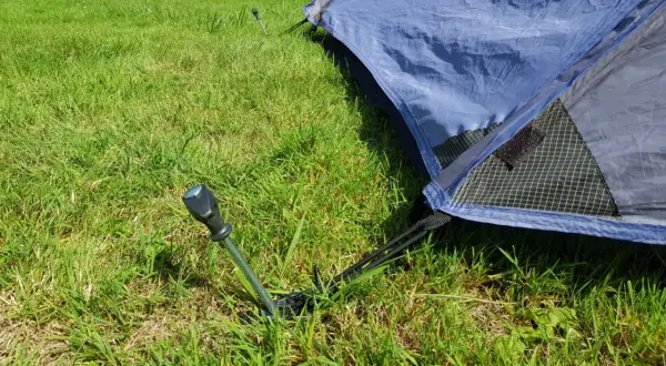 Ein Zelt wird mit Heringen im Gras abgespannt. Ein Hering ragt aus dem Boden, um das Zelt zu sichern.