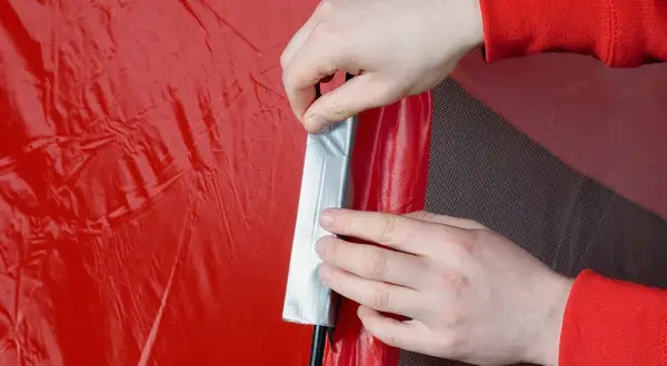 Hände reparieren mit Klebeband eine rote Zeltplane.