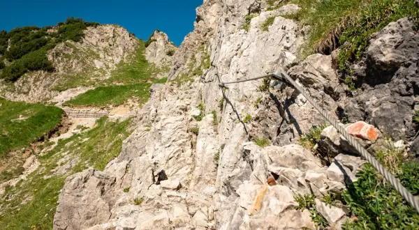 Auf einer steilen Felswand mit Seilsicherung für die rubihorn wanderung. Grüne Hänge und blauer Himmel.