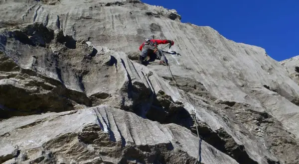 Marcel Dettling klettert eine steile Felswand empor, gesichert durch ein Seil. Der blaue Himmel bildet einen starken Kontrast zum grauen Gestein.