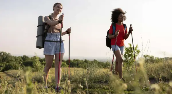 Zwei Frauen genießen eine 10 km Wanderung gesund in der Natur. Sie tragen Rucksäcke und Trekkingstöcke.