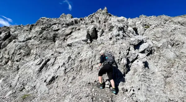 Frau klettert einen steilen Felsgrat im 3. Grad. Der Himmel ist strahlend blau.