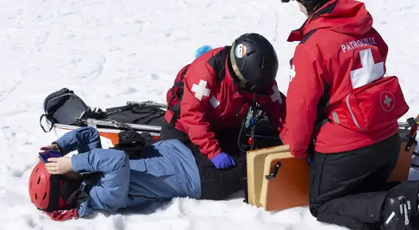 Bergretter kümmern sich nach einem Sturz auf Knie um einen verletzten Skifahrer im Schnee.