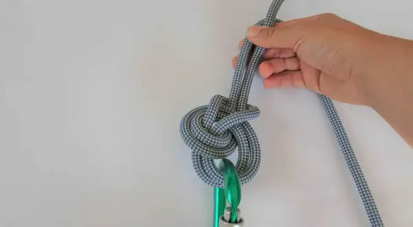 Hand hält ein Seil, das zu einem dicken Knoten gebunden ist, der an einem Karabiner befestigt ist.