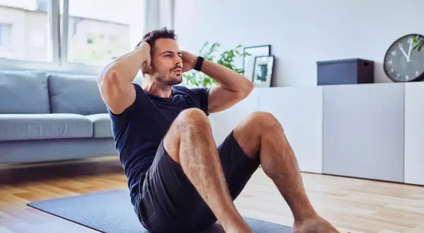 Mann macht Sit-ups auf einer Matte. Er trainiert trotz eines möglichen Rippenbruchs, um fit zu bleiben.