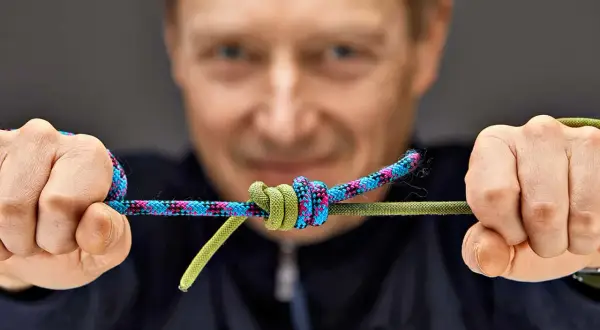 Mann zeigt einen Knoten an zwei Seilen. Eine detaillierte Knoten Anleitung für Bergsteiger.