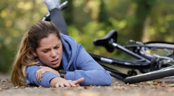 Junge Frau nach einem Sturz auf den Brustkorb, Fahrrad liegt daneben. Sie hält sich den Arm und hat Schmerzen.