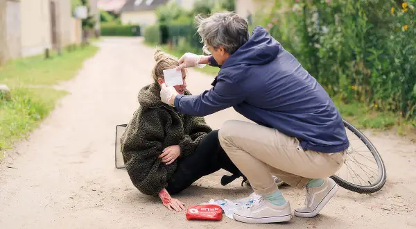 Erste Hilfe nach einem Sturz: Ein Mann versorgt eine Frau mit aufgeschürfter Hand und einem Verband am Auge.