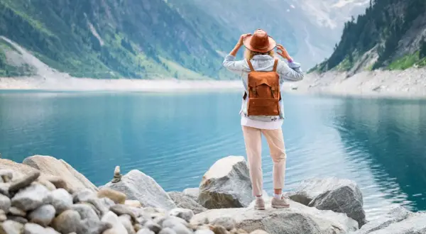 Frau mit Rucksack und Hut steht am Ufer eines türkisfarbenen Sees in den Bergen. Ein malerischer Ausblick, wie man ihn in Seen Deutschland findet.