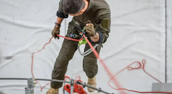 Mann in Uniform übt das Abseilen nur mit Seil. Er hält das Seil fest und kontrolliert den Abstieg.