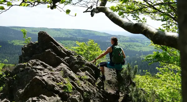 Frau mit Rucksack auf Felsen, genießt Aussicht auf bewaldete Hügel. Perfekt für eine 3 Tage Wanderung Deutschland.