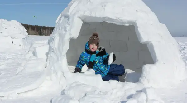 Kind im selbstgebauten Iglu, bereit für Winterabenteuer.