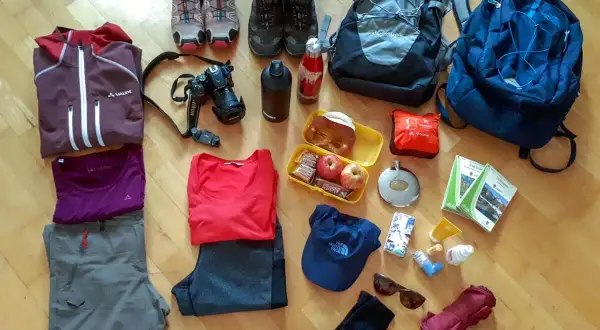 Packliste Wandern Mehrtagestour: Kleidung, Rucksäcke, Kamera, Verpflegung, Trinkflasche, Schuhe, Hut, Sonnenbrille, Regenschirm und Karten für die Tour.