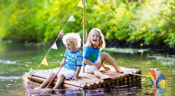 Zwei Kinder bauen einen Floss und genießen den Sommer auf dem Wasser.