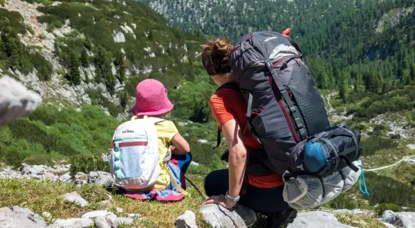 Mutter und Kind genießen die Aussicht beim steinernes Meer wandern. Die beiden sitzen auf einem Felsen, umgeben von grüner Natur und Bergen.