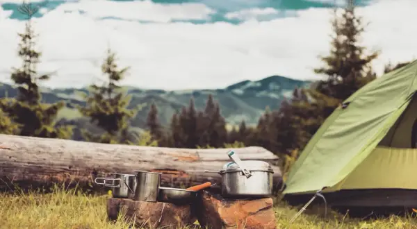 Campingausrüstung im Wald: Töpfe, Tasse und ein Zelt. Hier darf man im Wald schlafen und die Natur genießen.