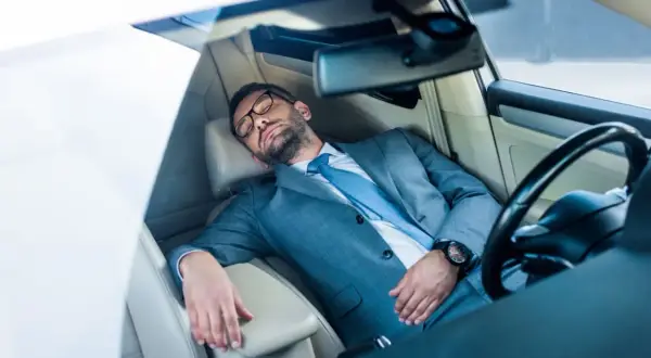 Mann im Anzug schläft im Auto. Ob man in Italien im Auto schlafen darf, ist eine andere Frage.