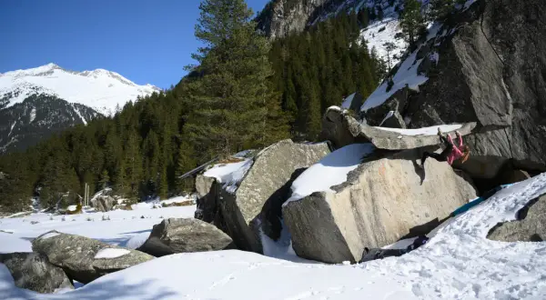 Eine Person klettert an einem Felsen im verschneiten Zillertal. Bouldern im Schnee ist eine Herausforderung!