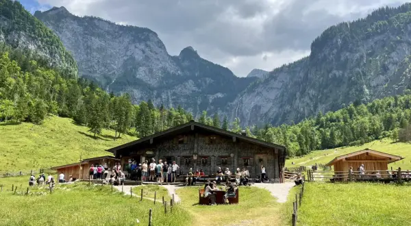 Eine Berghütte mit Gästen vor einer beeindruckenden Bergkulisse, die an ein steinernes Meer erinnert.