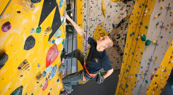 Mann klettert an einer gelben Wand mit bunten Griffen. Verschiedene klettern arten sind hier möglich.
