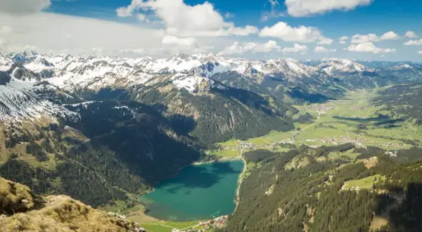 Blick ins Tannheimer Tal mit türkisfarbenem See, grünen Wäldern und schneebedeckten Gipfeln. Entdecken Sie hier Tannheimer Tal Geheimtipps!