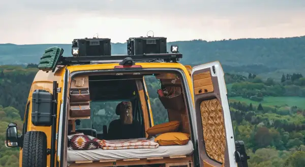 Gelbes Campervan mit gemütlichem Innenraum, bereit für wildcampen in Europa. Dachgepäckträger, Ersatzrad und Stauraum für Abenteuer.