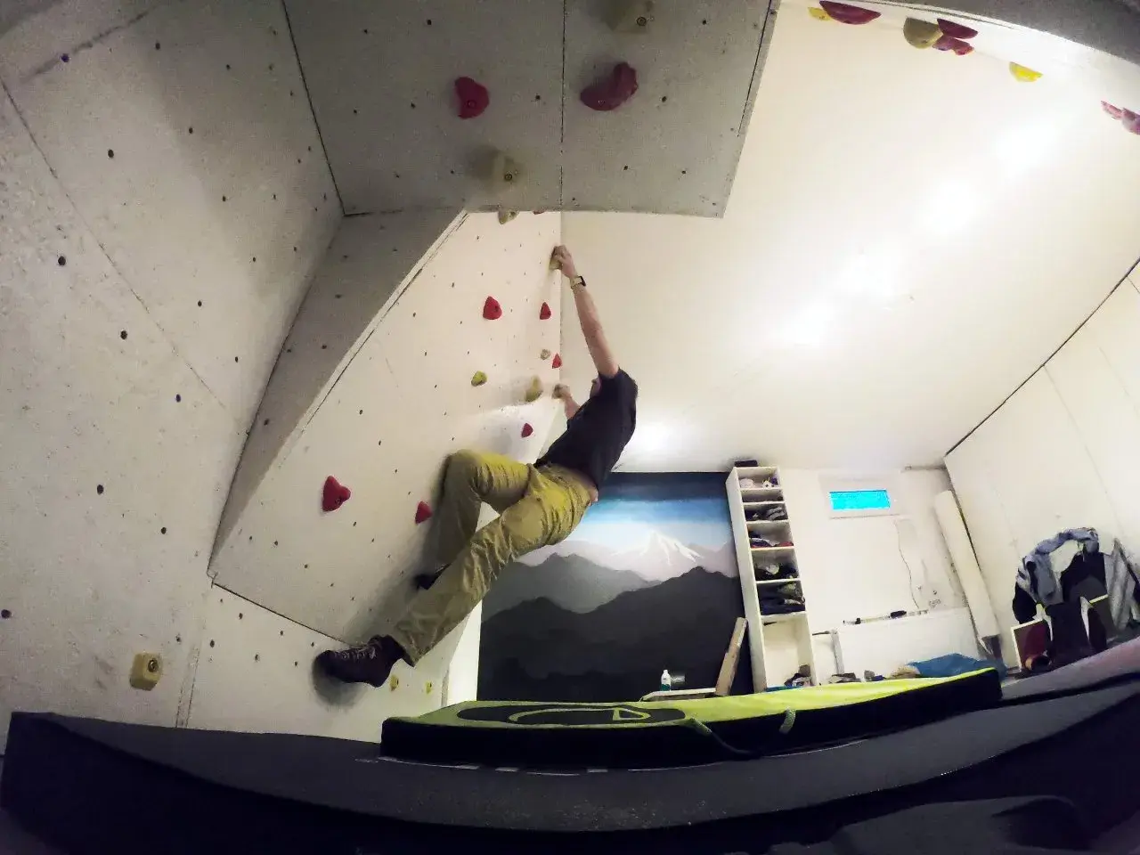 Mann klettert an einer selbstgebauten Boulderwand. Bunte Griffe sind auf der Wand verteilt.