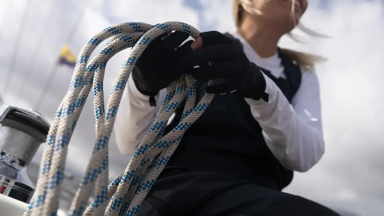 Seglerin mit Handschuhen hält ein dickes Seil. Die Knotentechnik Seil ist entscheidend für die Sicherheit auf See.