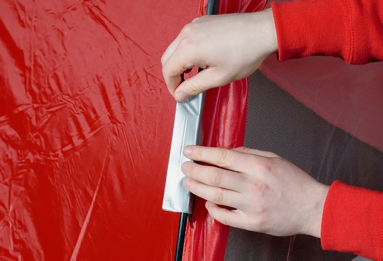 Hände reparieren mit Klebeband eine rote Zeltplane.