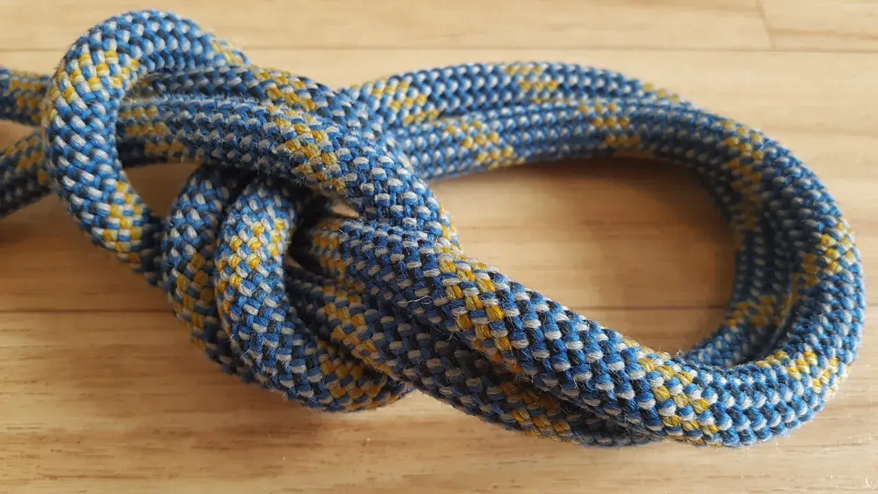 Ein blauer und gelber Kletterseilknoten, der als doppelter Bulin bekannt ist, liegt auf einem Holztisch.