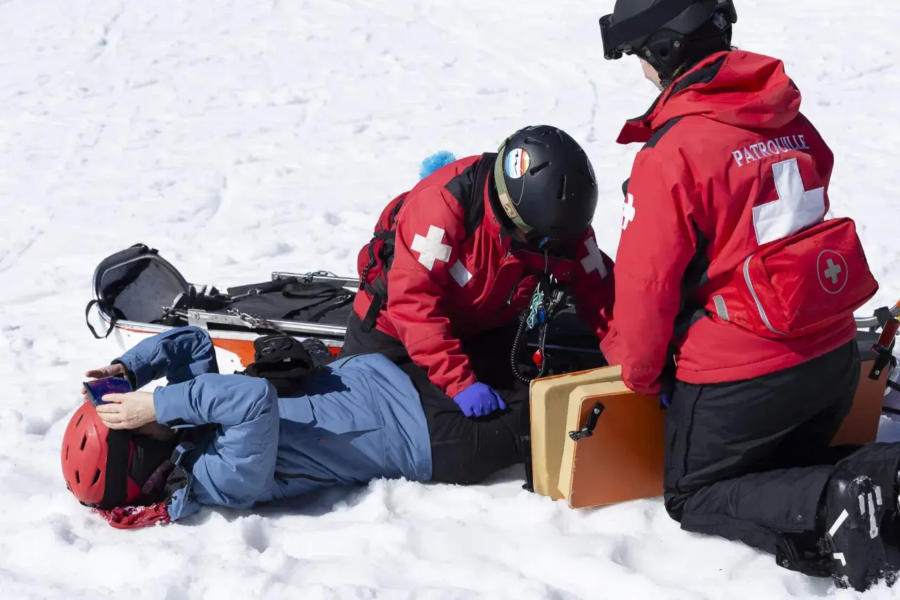 Bergretter kümmern sich nach einem Sturz auf Knie um einen verletzten Skifahrer im Schnee.
